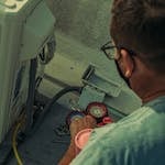 Professional technician repairing an outdoor air conditioning unit with gauges and tools.